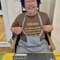 der Musiker sitzt mit Perücke und lustigem Sprüche-T-Shirt auf einem Stuhl