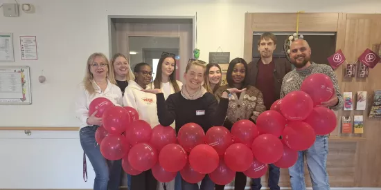 Neun Menschen halten eine Luftballongirlande